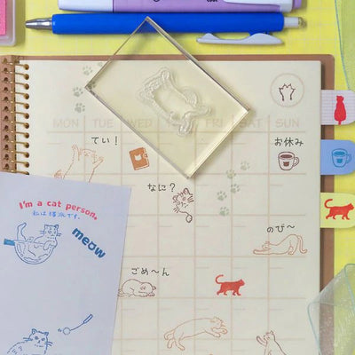 Stationery items including a notebook, pens, and a stamp with cat designs on a yellow background.