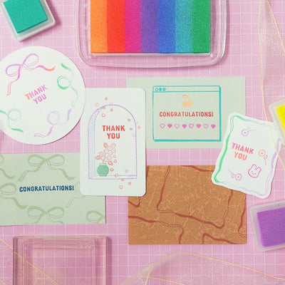 Colorful greeting cards and stamp pads on a pink grid background