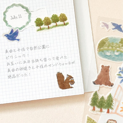 Notebook with nature-themed stickers including trees, a bird, a bear, and a squirrel.