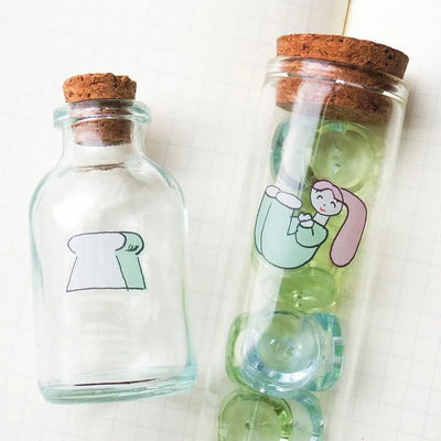 Two glass bottles with cork lids, one featuring a cartoon character and the other with a simple design.