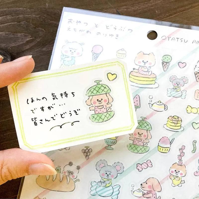 Hand holding a small card with cartoon character and text, with a sheet of more stickers in the background.