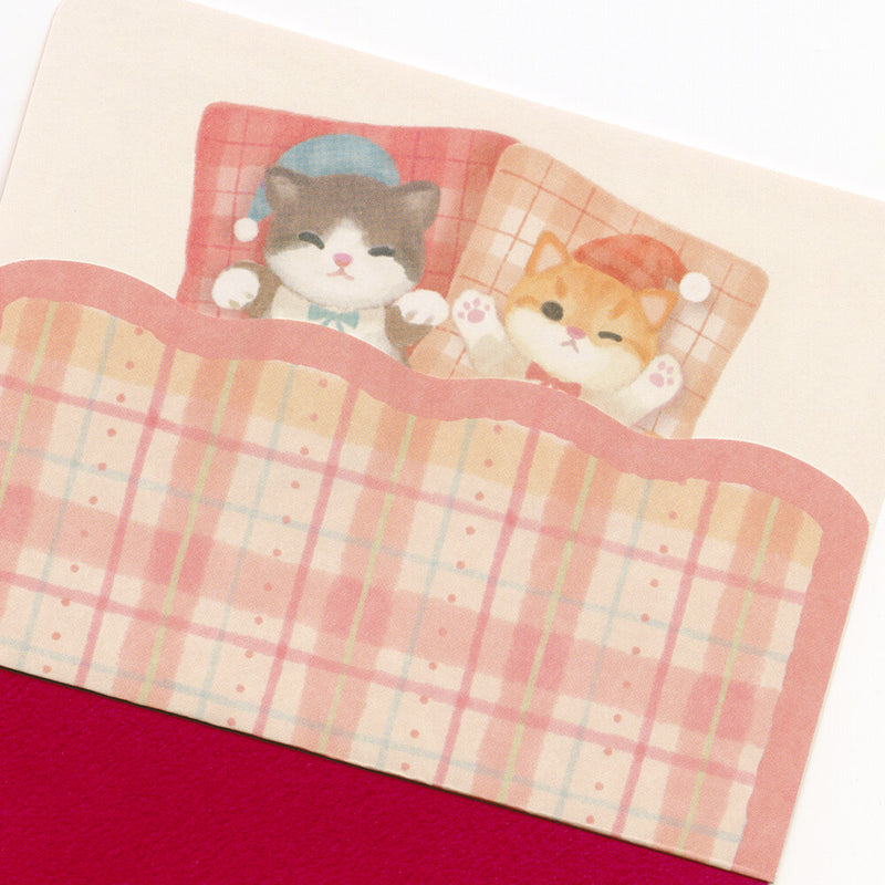 Two cartoon cats in a plaid bed with a red blanket