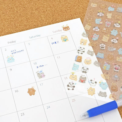 Calendar sheet with cute animal stickers and a blue pen on a cork background