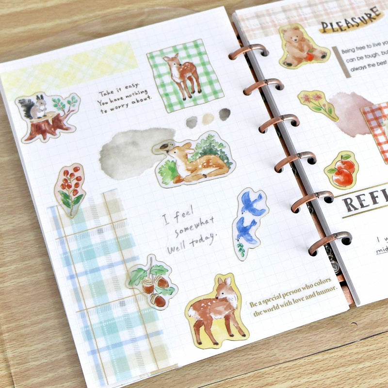 Open planner with decorative stickers featuring animals and text on a wooden surface