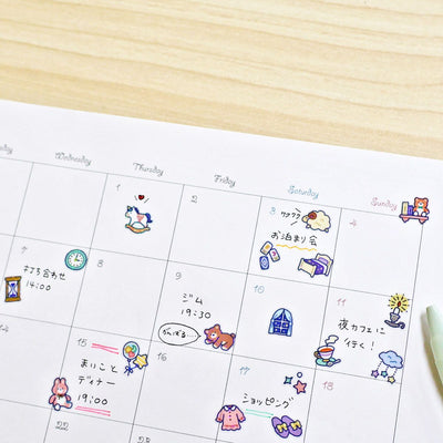 Calendar with cartoon icons and Japanese text on a wooden surface