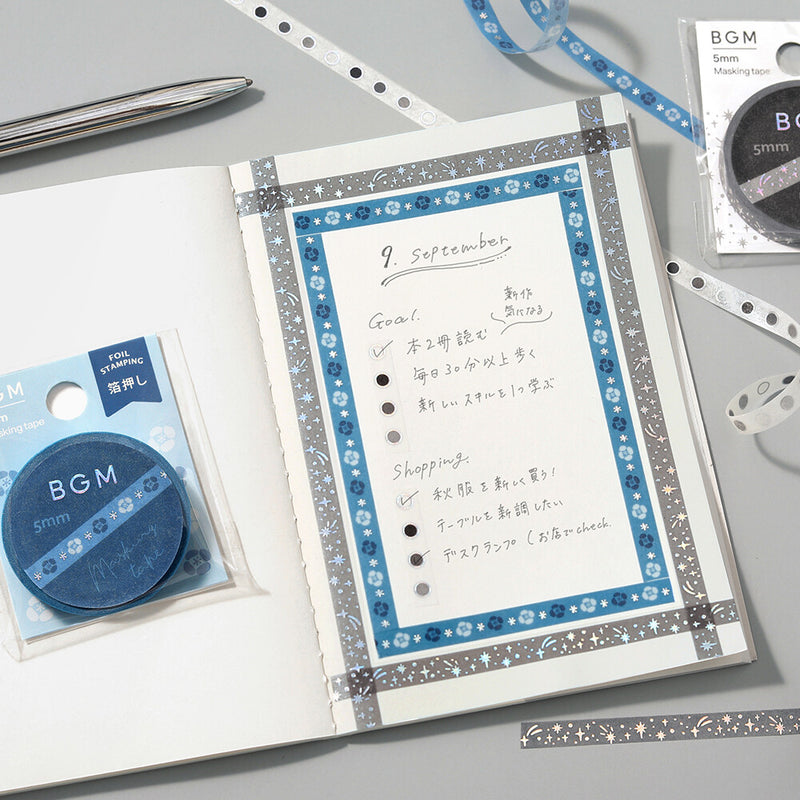 Notebook with decorative border, pen, and BGM products on a gray surface