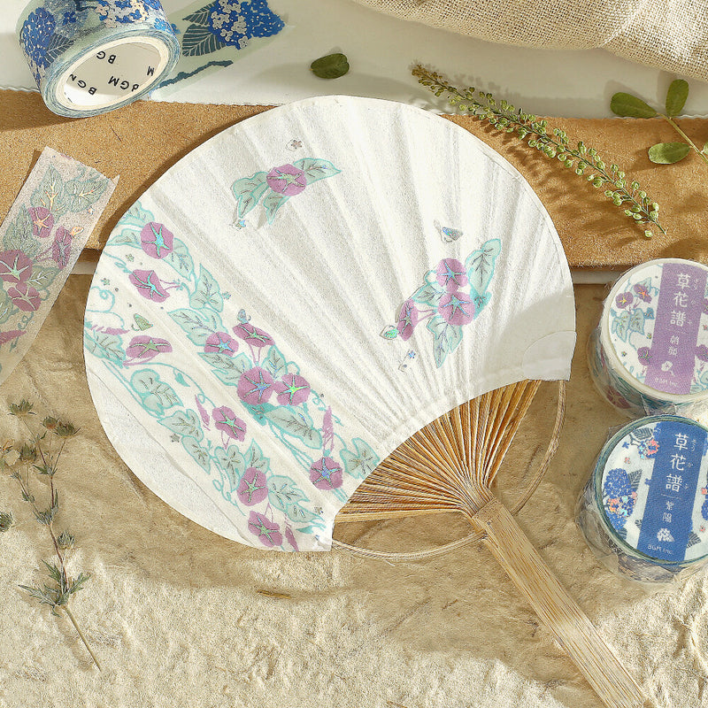 Floral-patterned hand fan on a textured surface with decorative tapes.