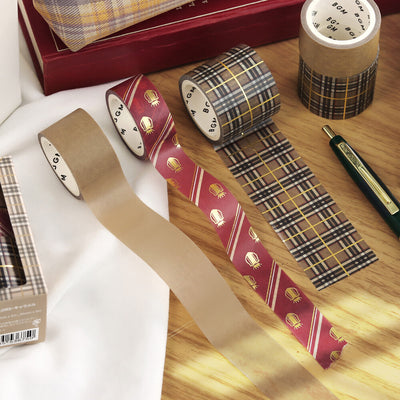 Plaid-patterned tape rolls on a wooden surface with a pen and box in the background.
