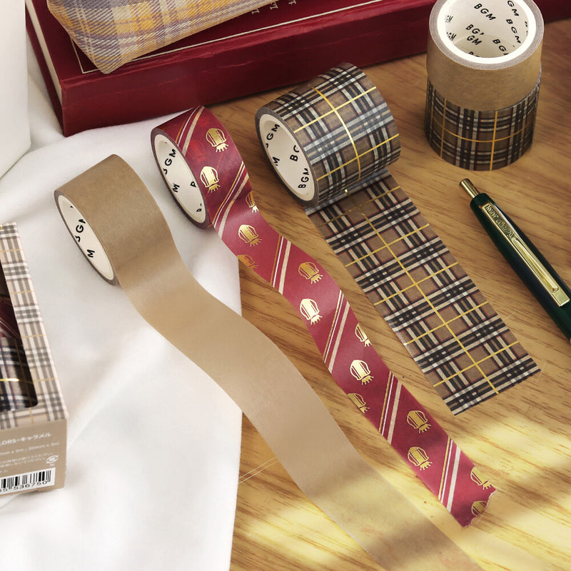 Plaid-patterned tape rolls on a wooden surface with a pen and box in the background.