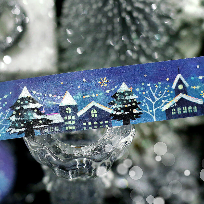 Decorative winter scene tape with houses and trees on a blue background, held over a glass container.