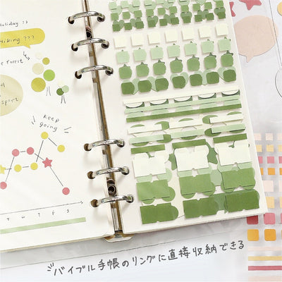 Planner with green sticky notes and decorative elements on a white surface