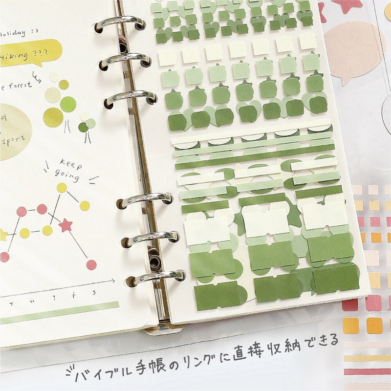 Planner with green sticky notes and decorative elements on a white surface