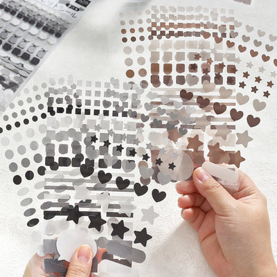 Hand holding a sheet of decorative stickers with various shapes and patterns on a white background.
