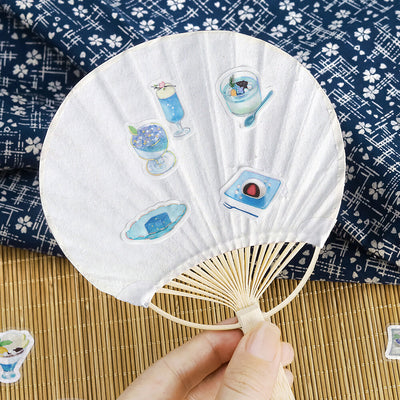 Handheld fan with decorative stickers on a blue floral fabric background