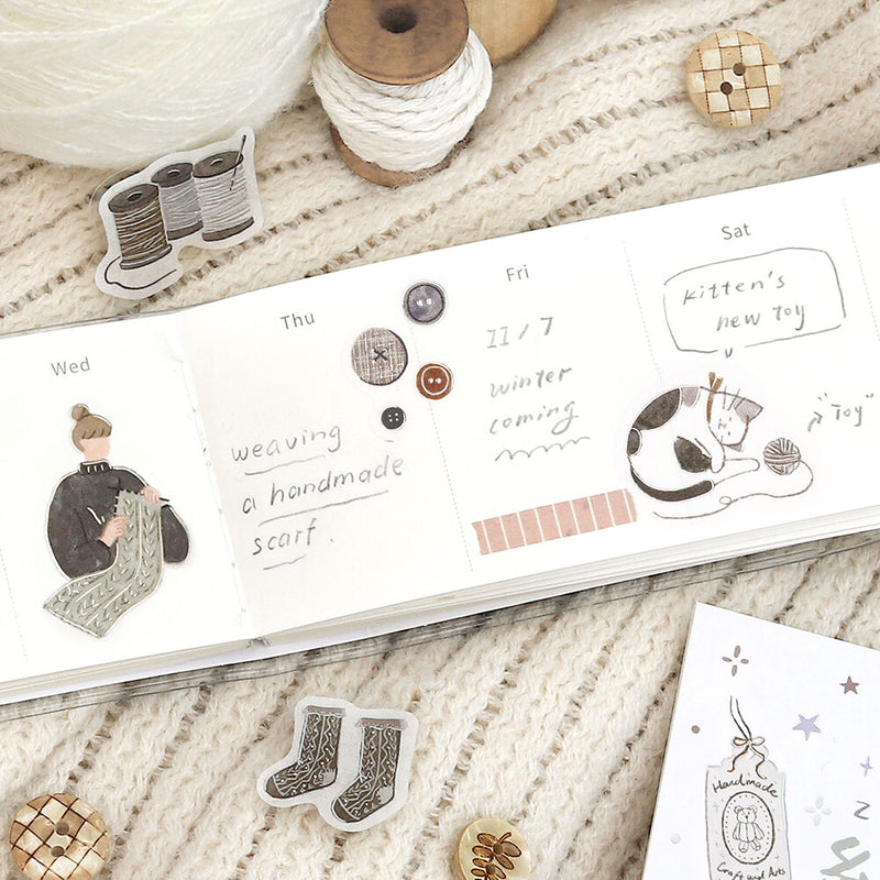 Notebook with hand-drawn illustrations and text on a textured surface with yarn and buttons.