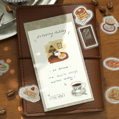 Brown leather notebook with a decorative card featuring illustrations of food and coffee on a wooden surface.
