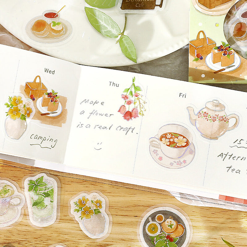 Weekly planner with illustrated stickers of tea, flowers, and food on a wooden surface.